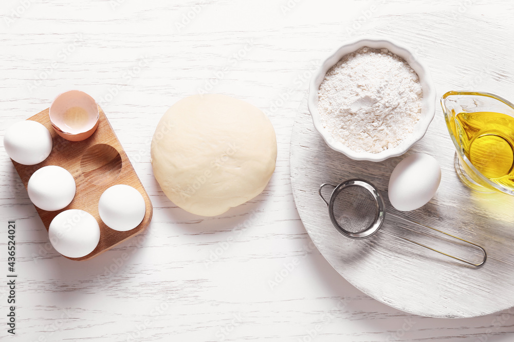 Fresh dough, flour, eggs and oil on light wooden background