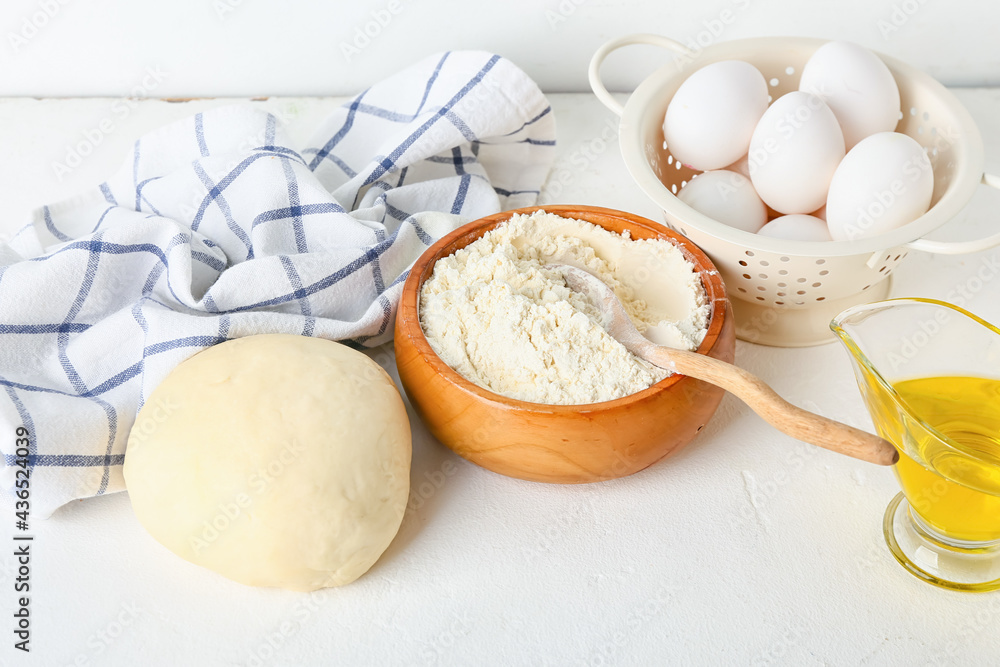 Bowl with fresh dough, flour, eggs and oil on light background