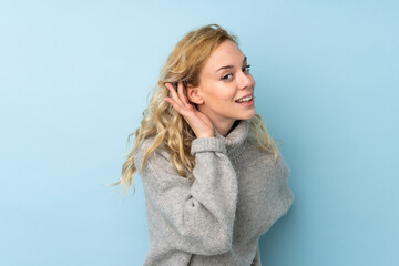 Poster - Young blonde woman wearing a sweater isolated on blue background listening to something by putting hand on the ear