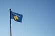 Kosovo flag hoisted on a flagpole waving in the wind. Low angle view against blue sky with plenty of copy space. 