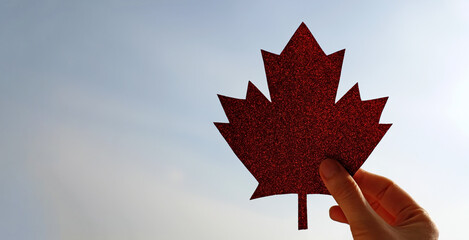 Maple leaf made of paper in the hand on blue sky background, Happy Canada Day. Copy space