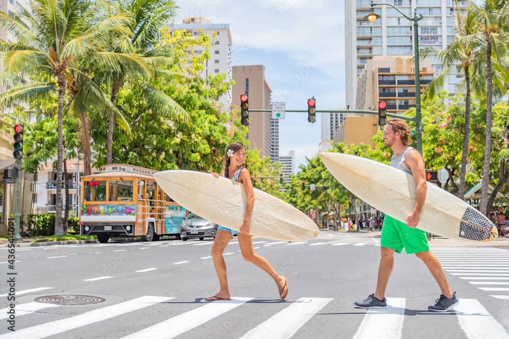 Honolulu Hawaii surfers couple tourists people walking crossing city street carrying surfboards going to the beach surfing. Surf living lifestyle. Surfer woman and man friends in Waikiki, Oahu, USA. - obrazy, fototapety, plakaty 