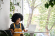 © insta_photos - Young happy African American college student hipster girl with afro hair sitting at table in cafe indoor alone using laptop watching learning virtual online digital webinar.