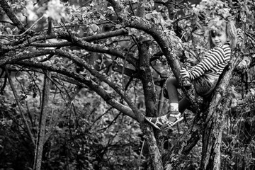 Wall Mural - A five-year-old girl sits in the branches of a tree in the garden. Black and white photo.