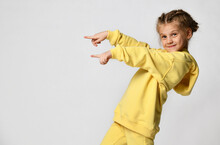 Joyful Active Little Girl Pointing Finger On An Empty Seat For The Text. Happy Cute Child In A Yellow Tracksuit On A White Background. Sportswear Advertising Concept. Banner.