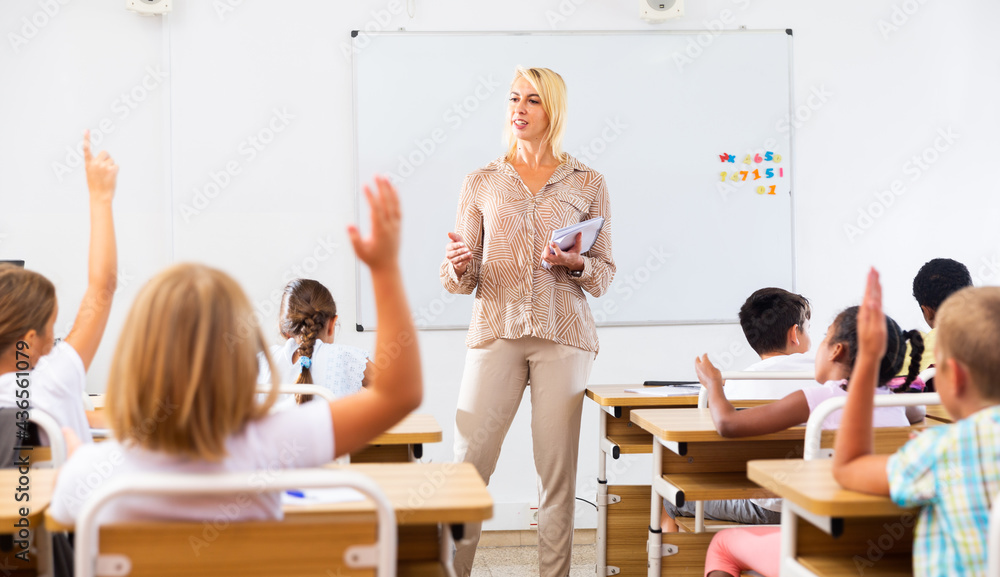 Woman teacher explaining studying material to tweens during lesson in elementary school, - obrazy, fototapety, plakaty 