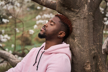 Man leaning on the tree with closed eyes and resting at the nature