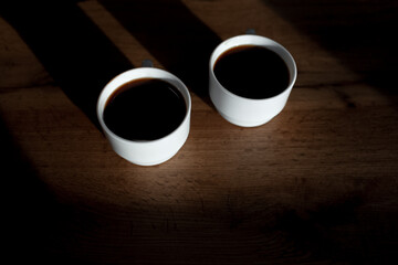 Top view of two white cups of coffee on wooden table.