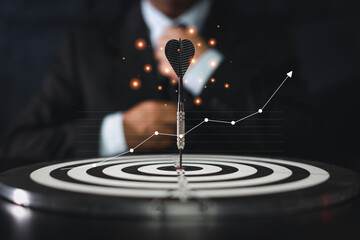 Businessman hands in suite sitting and controlling dart put to centre of target board with growth graph chart on vintage table meaning of investment and achievement goal. Planning and strategy concept