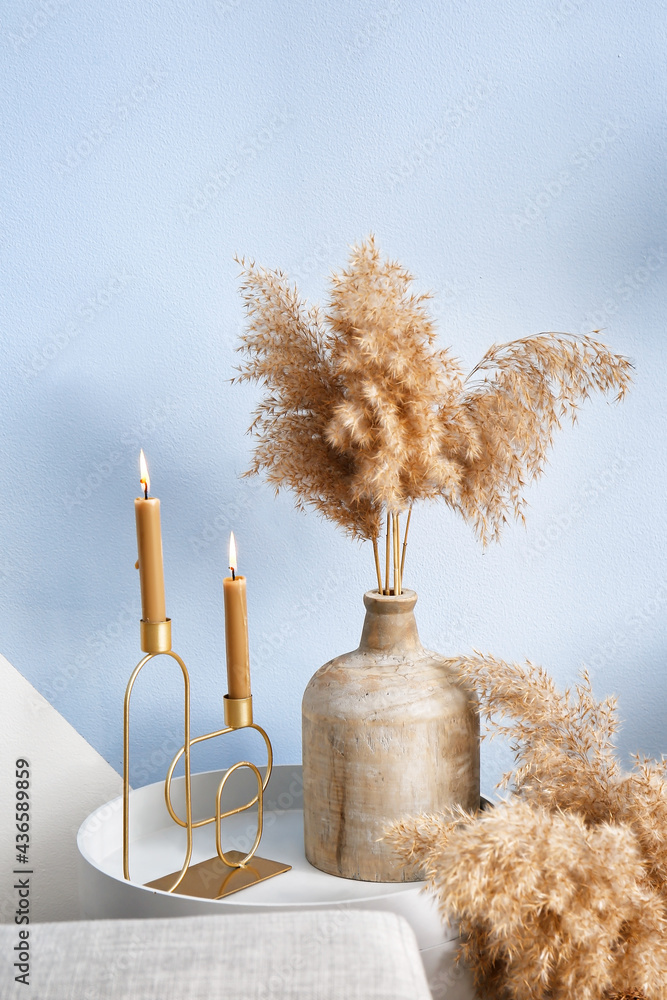 Burning candles and vase on table near color wall