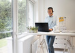 © epiximages - Man stands behind high table and speaks with headset and is working on laptop, notebook, pc