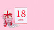 © Alena - A gift box in a shopping trolley, dollars and a calendar with the date of 18 june on a pink background.