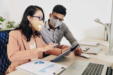 Wall Mural - serious businesswoman in protective mask and glasses showing presentation of her idea on tablet comp