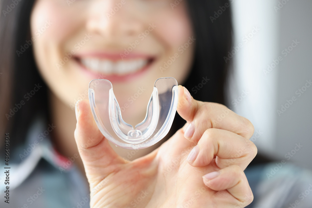 Smiling woman holds transparent plastic mouth guard in her hand - obrazy, fototapety, plakaty 