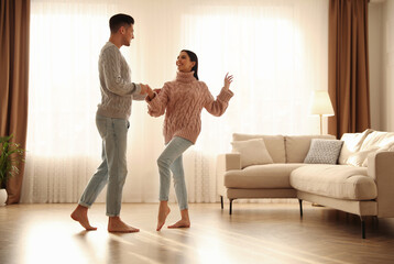 Canvas Print - Happy couple dancing barefoot in living room. Floor heating system