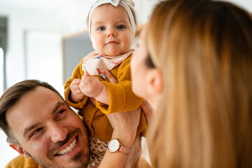 Wall Mural - Proud mother and father smiling at their baby daughter at home