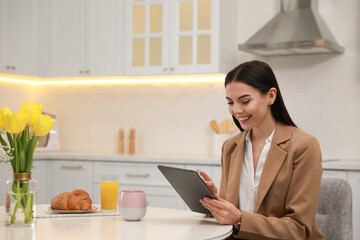 Canvas Print - Young woman with tablet having breakfast in kitchen. Morning routine