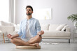 Young man meditating on straw cushion at home, space for text