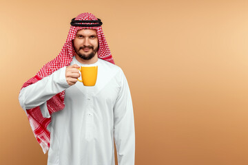 Wall Mural - A man Arab holds in a national costume holds a mug in his hand on a beige background. Oriental hospitality concept.