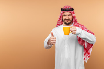 Wall Mural - A man Arab holds in a national costume holds a mug in his hand on a beige background. Oriental hospitality concept.