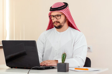 Wall Mural - An Arab man, a businessman, a sheikh works at a laptop. Investments, business, work via the Internet, online contracts.