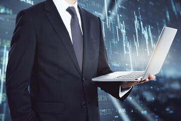 Poster - Young european businessman with laptop, glowing forex chart and map hologram standing on blurry office background. Finance concept. Double exposure.