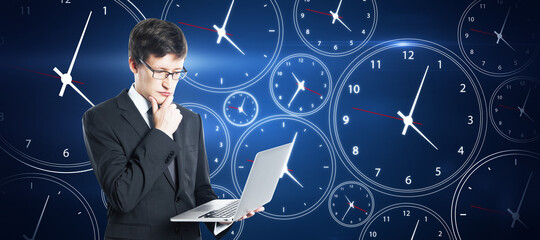 Time management concept. Pensive young european businessman with laptop on creative blue clock background.