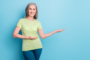 Canvas Print - Photo of attractive cheerful old woman hold hands empty space decide product isolated on blue color background