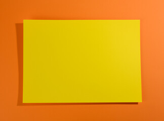 Wall Mural - blank yellow sheet of paper on orange background with shadow