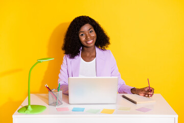 Poster - Photo of young happy positive smiling afro woman working in laptop writing in organizer isolated on yellow color background