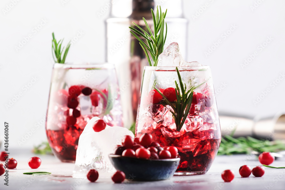 Cranberry, vodka, gin alcoholic cocktail with ice, rosemary and berries in tumbler glass. Summer long drink. Gray table background - obrazy, fototapety, plakaty 