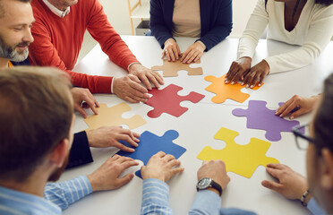 Collaboration concept. Diverse multiethnic people group team assembling jigsaw putting puzzle pieces together sitting at round office desk table represent team support during coaching training