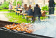 Barbecue fries in the coals. Blurred people eat at the table in the background. Meat and beef at the field kitchen festival.