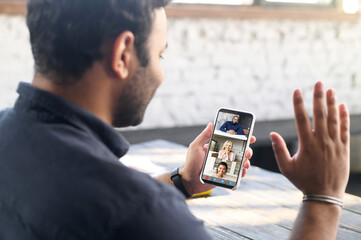 Indian guy using mobile app for video connection, holding smartphone and waving to online interlocutor, happy hindu guy enjoying chatting via video call, staying in touch with family on the distance