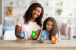 Portrait of black mother and her cute daughter showing eco-friendly garbage sorting board game at camera, indoors