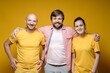 Friendly smiling bearded man hugs friends, man and woman. Yellow background.