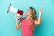 Young Brazilian woman isolated on blue background shouting through a megaphone to announce something in lateral position