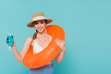 Wall Mural - Smiling woman holding cocktail and swim ring isolated on blue.