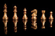 Golden chess include king queen horse ship and pawn on black background with reflection.