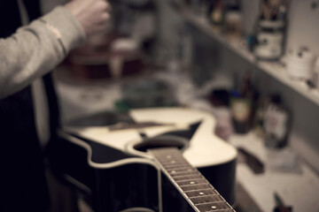 A service worker repairs a guitar with a tool.