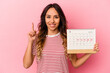 © Asier - Young mexican woman holding a calendar isolated on pink background showing number one with finger.