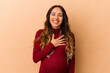 © Asier - Young mexican pregnant woman isolated on beige background laughs out loudly keeping hand on chest.