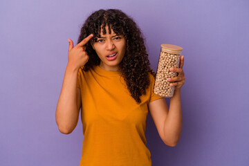 Wall Mural - Young brazilian woman holding a chickpea bottle isolated on purple background showing a disappointment gesture with forefinger.