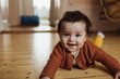 © Maskot - Portrait of smiling male toddler lying on floor at home