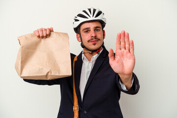 Young business caucasian man wearing bike helmet and holding take way food isolated on white background standing with outstretched hand showing stop sign, preventing you.