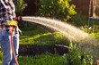 Female hands holding garden water hose wearing colorful wellies watering garden