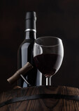 Fototapeta Panele - Red wine bottle with glass and vintage corkscrew on top of wooden barrel on black.