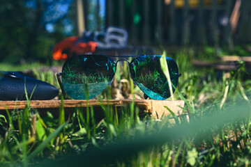 blue sunglasses on a background of green grass and a power saw