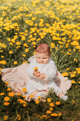 Baby girl sits on a field of dandelions on a sunny day. Vertical