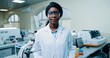 Close up portrait of happy positive young African American beautiful female medical scientist in goggles and white coat standing in clinic lab and smiling looking at camera Modern laboratory, medicine